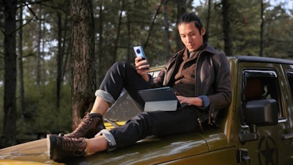 Mann sitzt mit HUAWEI Smartphone und HUAWEI MatePad auf einem gelben Auto im Wald