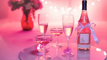 Champagnerflasche mit Gläsern vor rosa Hintergrund