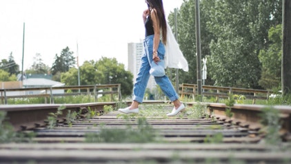 Frau in weiter Jeans überquert ein stillgelegtes Gleis